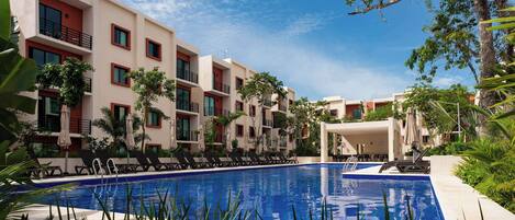 A swimming pool surrounded by modern buildings with balconies, some with red accents, and lush greenery.