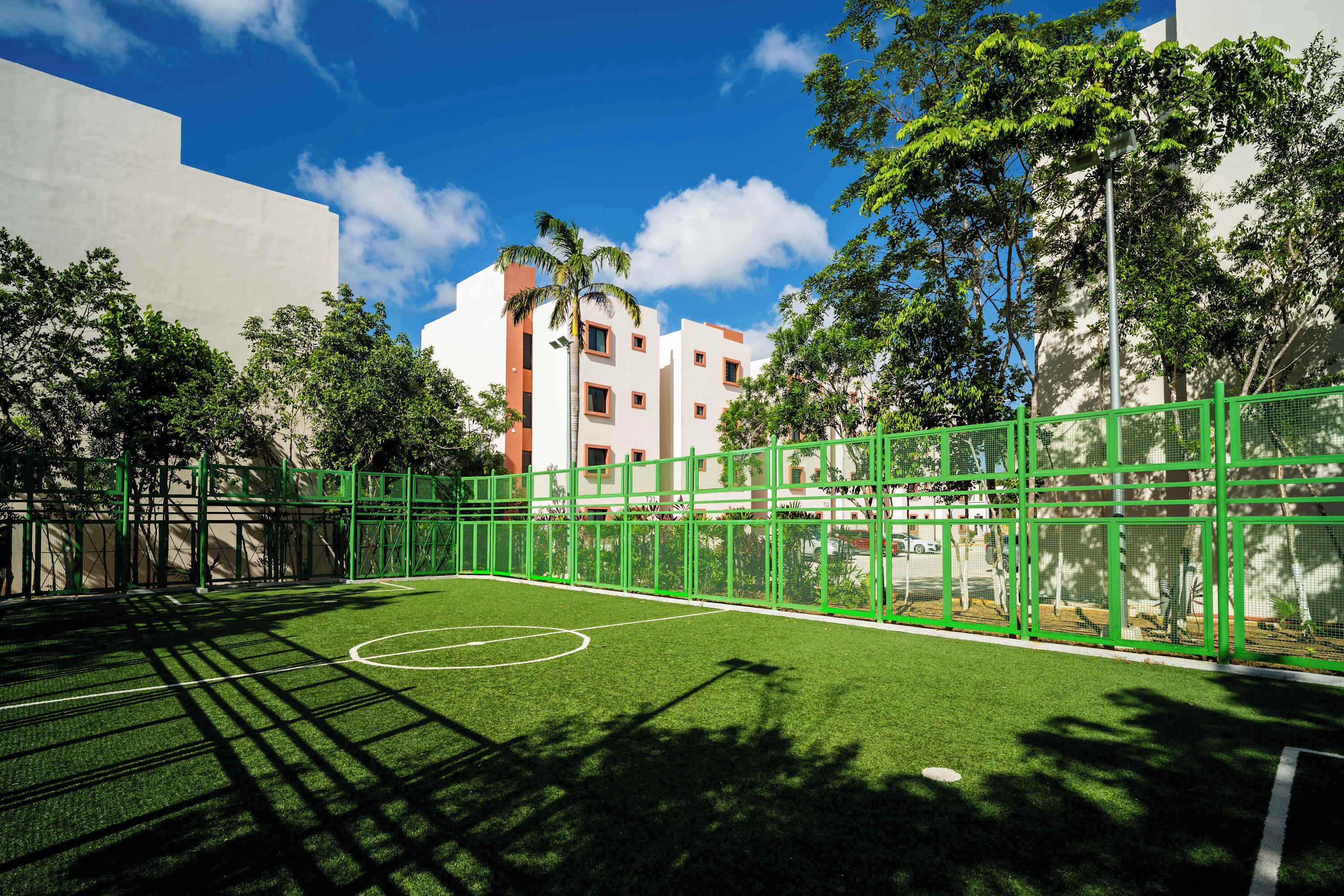 An outdoor sports court with a green fence, surrounded by trees and buildings.