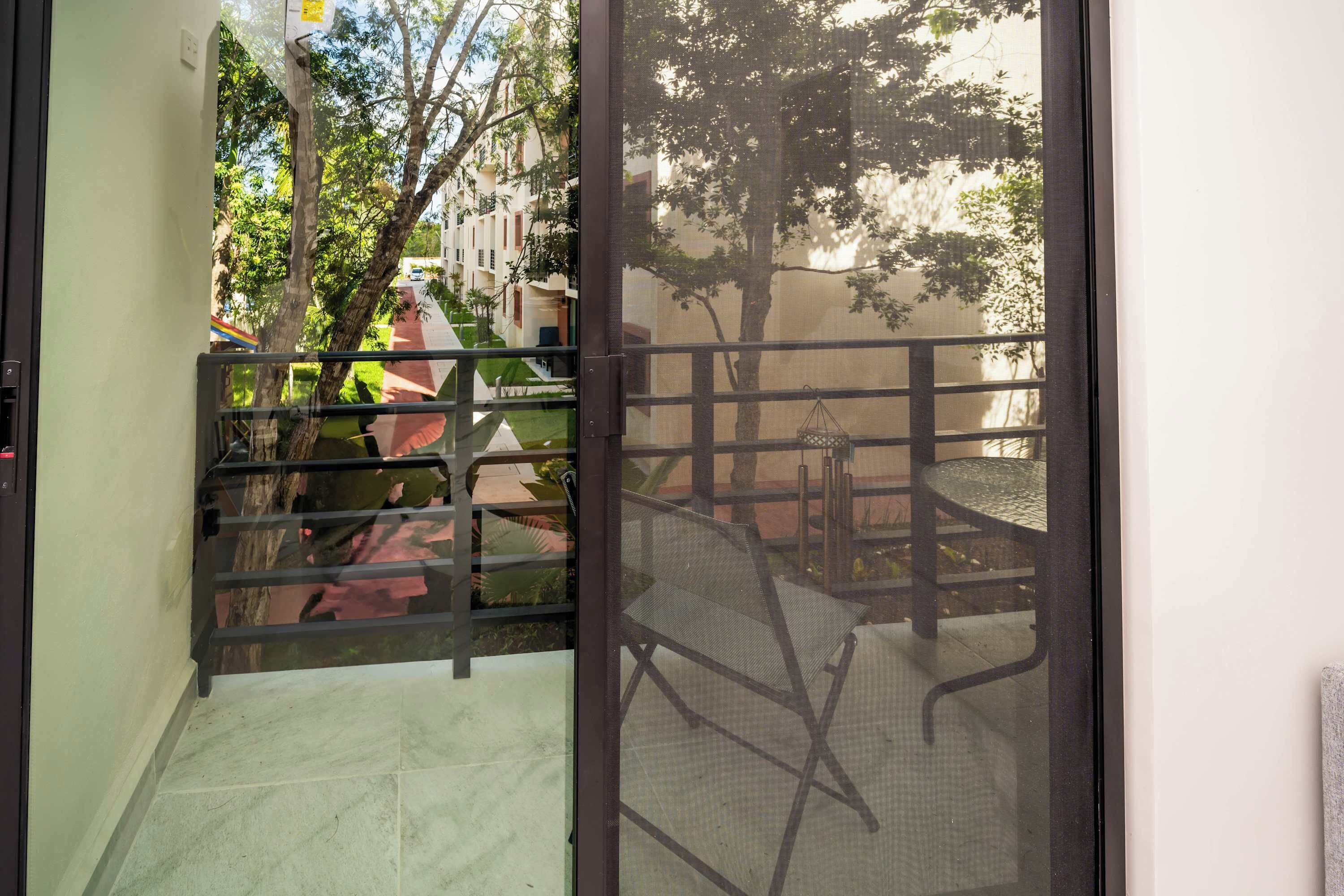 A view through a glass door with a metal gate leading to an outdoor area with a chair and a table.