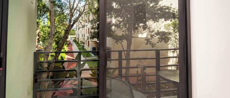 A view through a glass door with a metal gate leading to an outdoor area with a chair and a table.