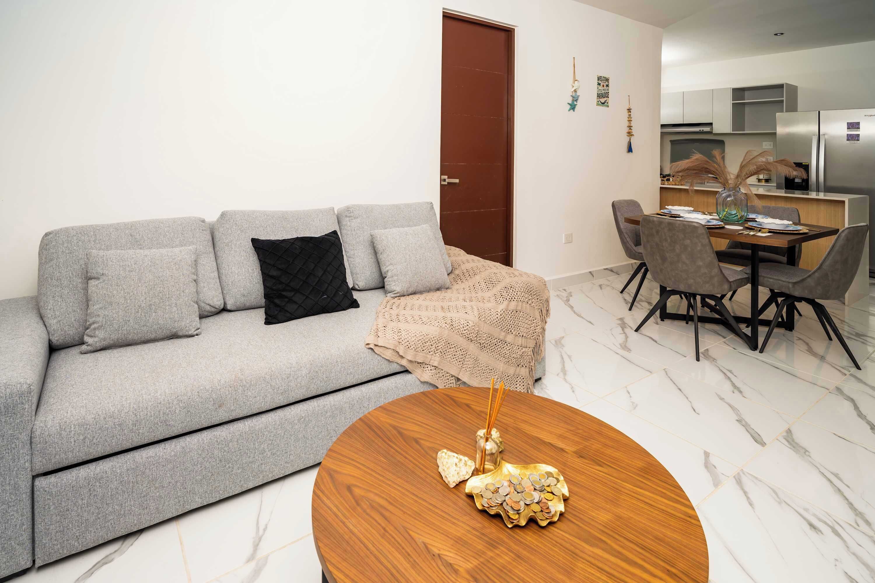 Un salon moderne avec un canapé gris, une table basse ronde en bois et un coin repas comprenant une table et des chaises.