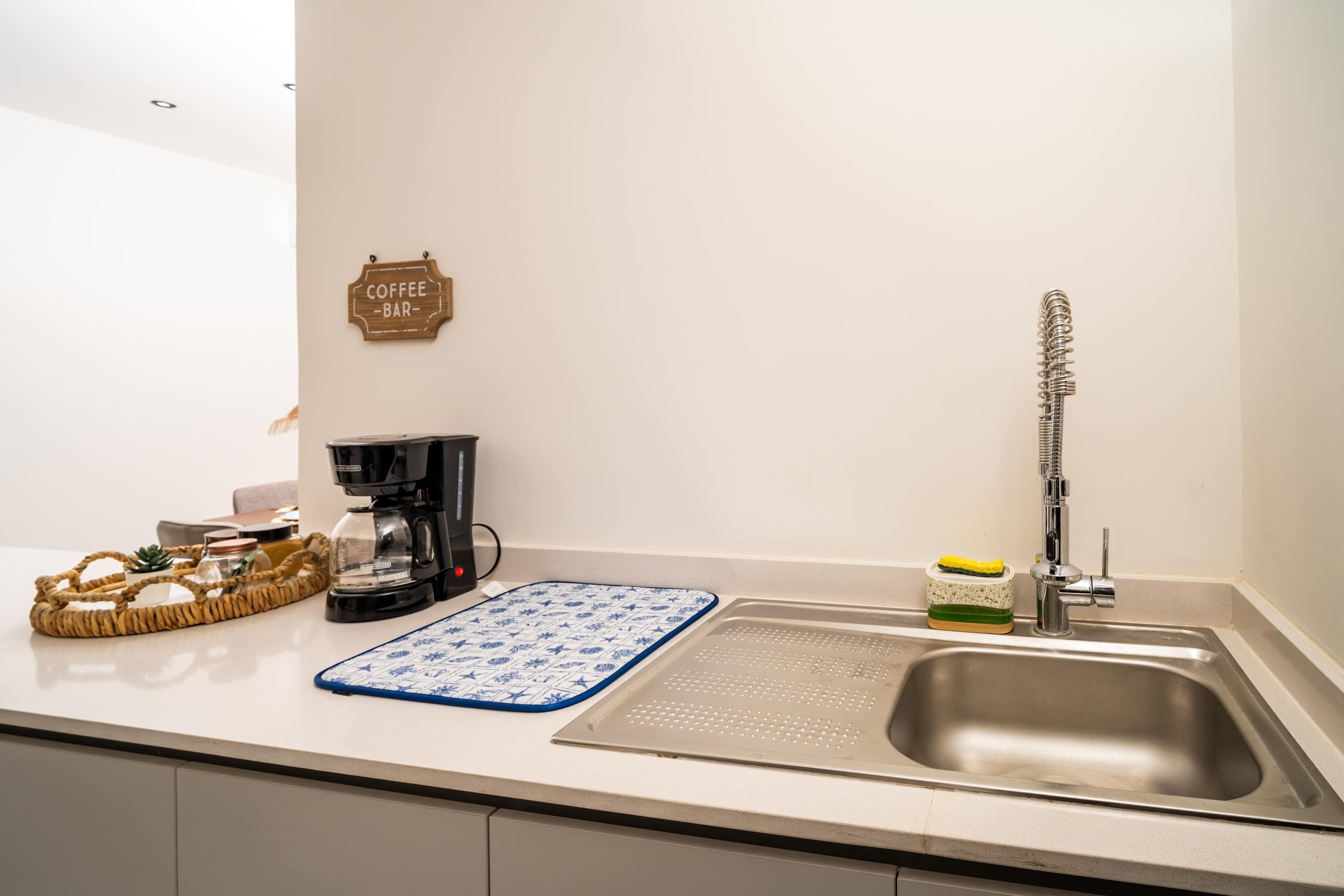 A kitchen with a coffee machine, a sink, a blue and white patterned mat, and a sign that reads "Coffee Bar".