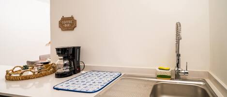 A kitchen with a coffee machine, a sink, a blue and white patterned mat, and a sign that reads "Coffee Bar".