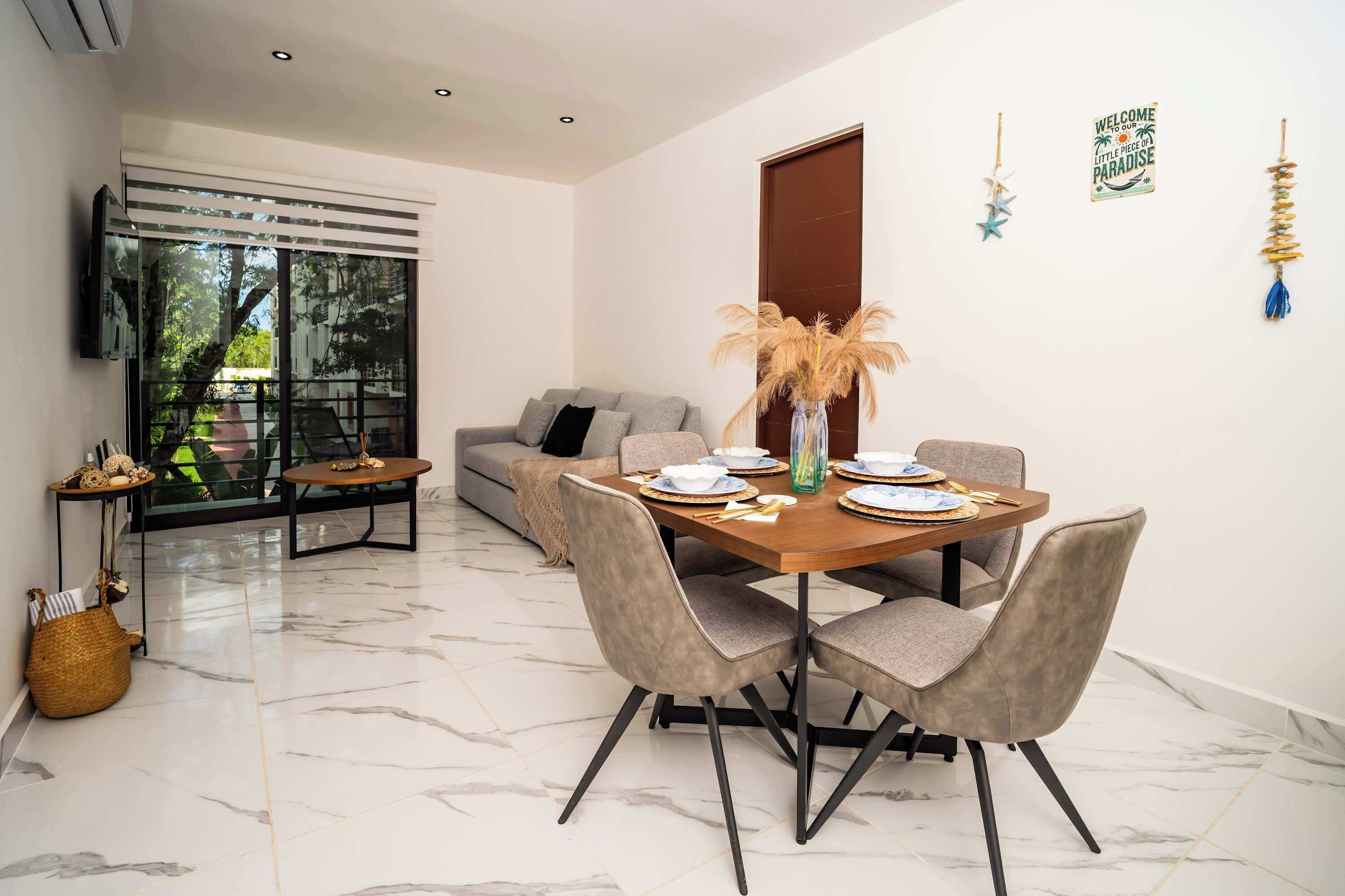 A modern dining area with a marble floor, a wooden dining table set for four, and a grey sofa in the background.