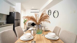 Un coin repas moderne avec une table en bois dressée pour quatre personnes, entourée de chaises de couleur beige. Un vase contenant des plumes d'herbe des pampas est placé au centre.
