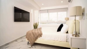 Une chambre d’hôtel moderne équipée d’un lit, d’une lampe de chevet, d’un téléviseur à écran plat et d’une grande fenêtre.