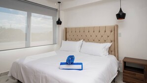 A neatly made bed with white linens, a blue towel, and a rolled-up towel on the bed. - Unique Studio at the Entrance of the Hotel Zone (Cancún)