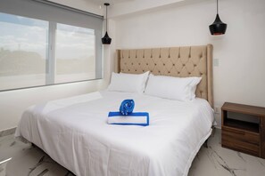 A neatly made bed with white linens, a blue towel, and a rolled-up towel on the bed.