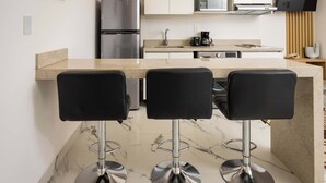 A modern kitchen with a marble countertop, stainless steel appliances, and three black bar stools. - Unique Studio at the Entrance of the Hotel Zone (Cancún)