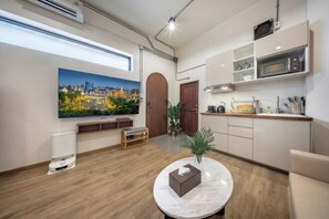 Ein modernes Hotelzimmer mit Holzboden, einem runden Marmortisch, einem großen Stadtbild und einer Küchenzeile. Eine Holzbank steht ebenfalls im Raum.
