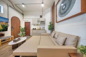 Ein modernes Wohnzimmer mit einer Couch, einem Esstisch und einer Küchenzeile im Hintergrund.