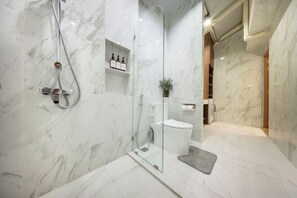 Ein modernes Badezimmer mit einer einteiligen Glasdusche, Toilette und Marmorwänden.