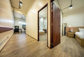 Ein Hotelzimmer mit Holzboden, einem Bett, einem Nachttisch, einem Spiegel und einer Tür zu einem anderen Raum.