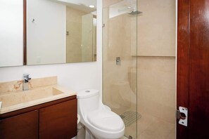 A bathroom with a glass-enclosed shower, a white toilet, and a marble sink.