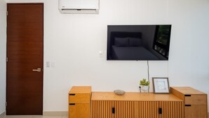 A modern living room with a wooden entertainment unit, a mounted TV, and a door. - Oceanview with Rooftop Pool in Playa Tortugas (Cancún)