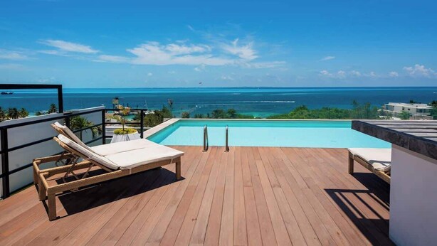 A wooden deck with a pool, lounge chairs, and a view of the ocean. - Oceanview with Rooftop Pool in Playa Tortugas (Cancún)