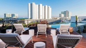 A rooftop lounge area with white lounge chairs, a small pool, and a view of tall buildings in the background. - Charming with pool, roof terrace and gym (Cancún)