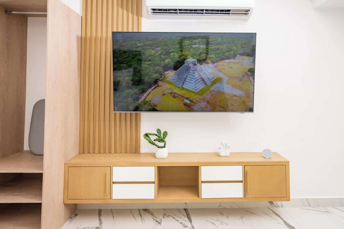 A modern living room with a wooden TV stand, a flat-screen TV mounted on the wall, and a small potted plant on the stand.