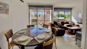 A dining area with a round table set for four, surrounded by wicker chairs. There is a sofa and a small table in the background. - Cozy Gym-Pool-3 floors (Cancún)
