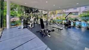 A modern gym with various exercise equipment, large windows, and indoor plants. - Cozy Gym-Pool-3 floors (Cancún)