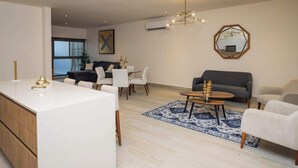 Una sala moderna con un sofá blanco, una mesa de comedor y una mesa de centro. Se ve una ventana grande al fondo.