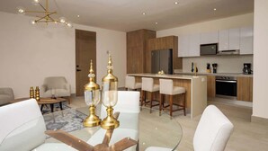 Una sala moderna con una mesa de centro de vidrio, sofás blancos y un comedor con una mesa de vidrio y candelabros dorados.