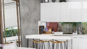 A modern kitchen with white cabinets, a bar area with stools, and a view of greenery outside. - Studio 9 - Luxury Apartment (Byron Bay)
