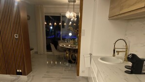 A modern kitchen with a marble countertop, a sink with a gold faucet, and a dining area with a chandelier.