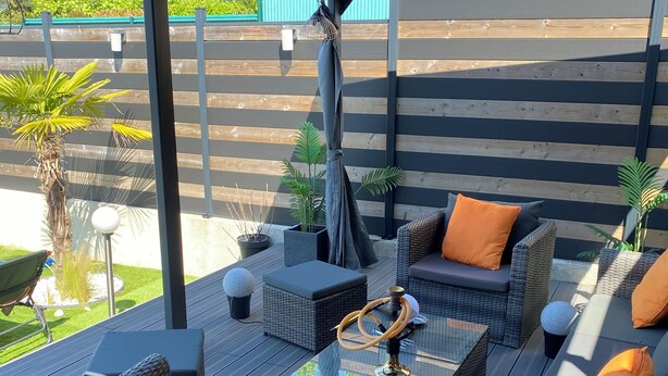 An outdoor patio with wicker furniture, a glass coffee table, and a hanging chair.
