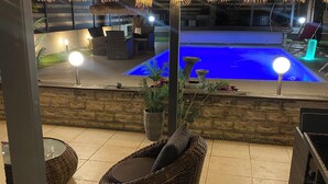 An outdoor patio area with wicker furniture, a swimming pool, and string lights.
