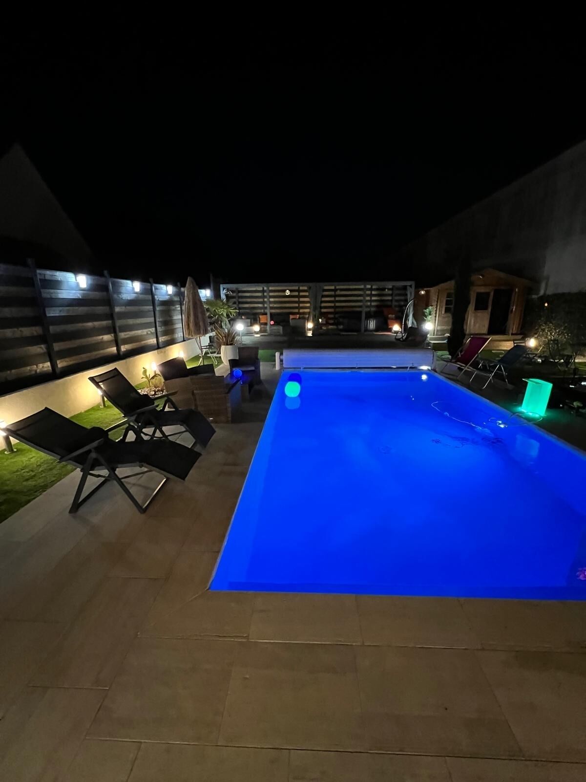 A swimming pool with blue lighting, surrounded by outdoor furniture and a covered area with lights.