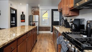 A modern kitchen with granite countertops, wooden cabinets, a stainless steel refrigerator, a gas stove, and a built-in oven.