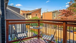 A wooden deck with a table and chairs, overlooking a backyard with a wooden fence and houses in the background.