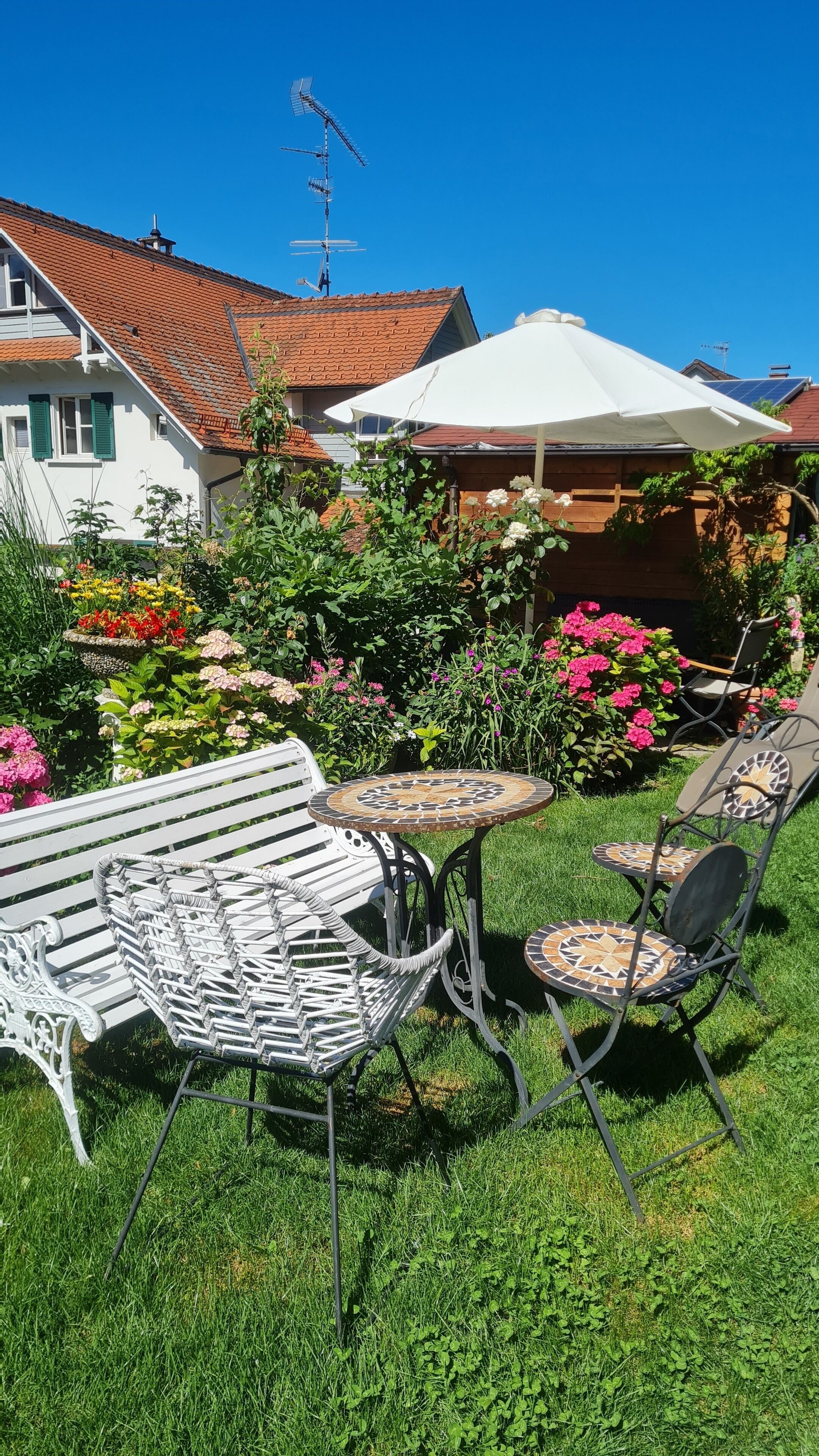 A garden with a white table and chairs, surrounded by lush greenery and colorful flowers.