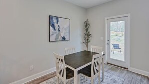 A dining area with a dark wooden table and white chairs, a painting on the wall, and a door leading to an outdoor area. - Entire 4 Bedroom home in Pearl, Mississippi (Pearl)