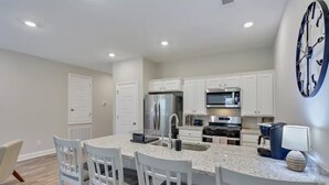 A modern kitchen with white cabinetry, stainless steel appliances, and a large island with bar stools. - Entire 4 Bedroom home in Pearl, Mississippi (Pearl)