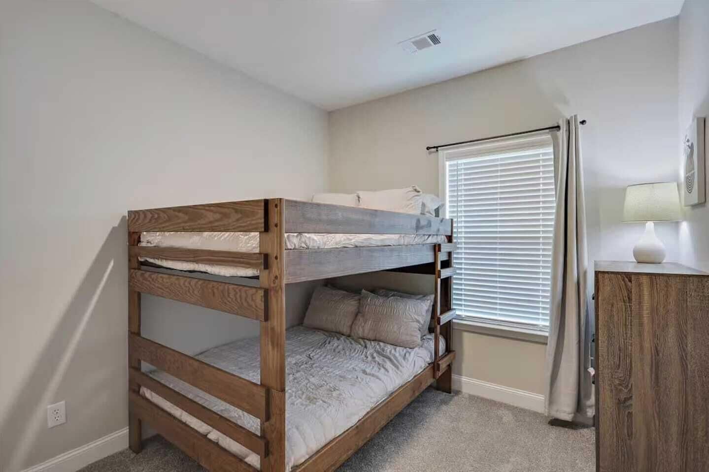 Un lit superposé dans une chambre avec une fenêtre, un bureau et une lampe.