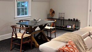 A cozy room with a dining table, two chairs, a bookshelf, and a sofa. - Refined Carriage Apartment in Historic Hope Valley (Durham)