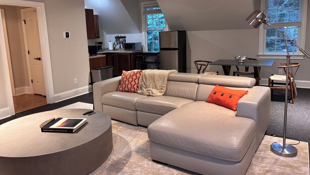 A modern living room with a sectional sofa, a round coffee table, and a dining area with a small table and chairs. - Refined Carriage Apartment in Historic Hope Valley (Durham)
