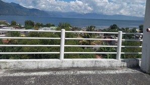 A view from a balcony with a railing, overlooking a coastal area with mountains in the distance and a clear sky. - Hotel Peneleu (San Pedro La Laguna)