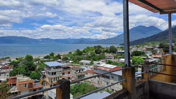 A coastal town with buildings, a view of the sea, and mountains in the background. - Hotel Peneleu (San Pedro La Laguna)