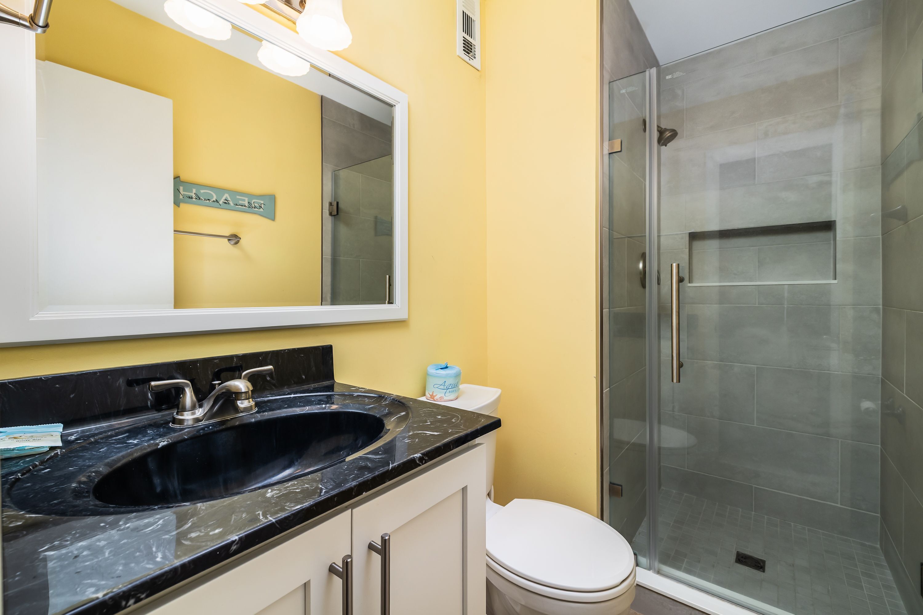 Une salle de bain avec un lavabo noir, un miroir, des toilettes et une douche à parois de verre.