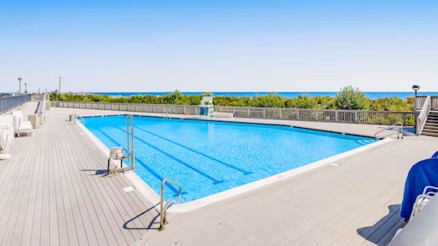 Una piscina con bordo in legno, una sedia per il bagnino e vista sull'oceano.