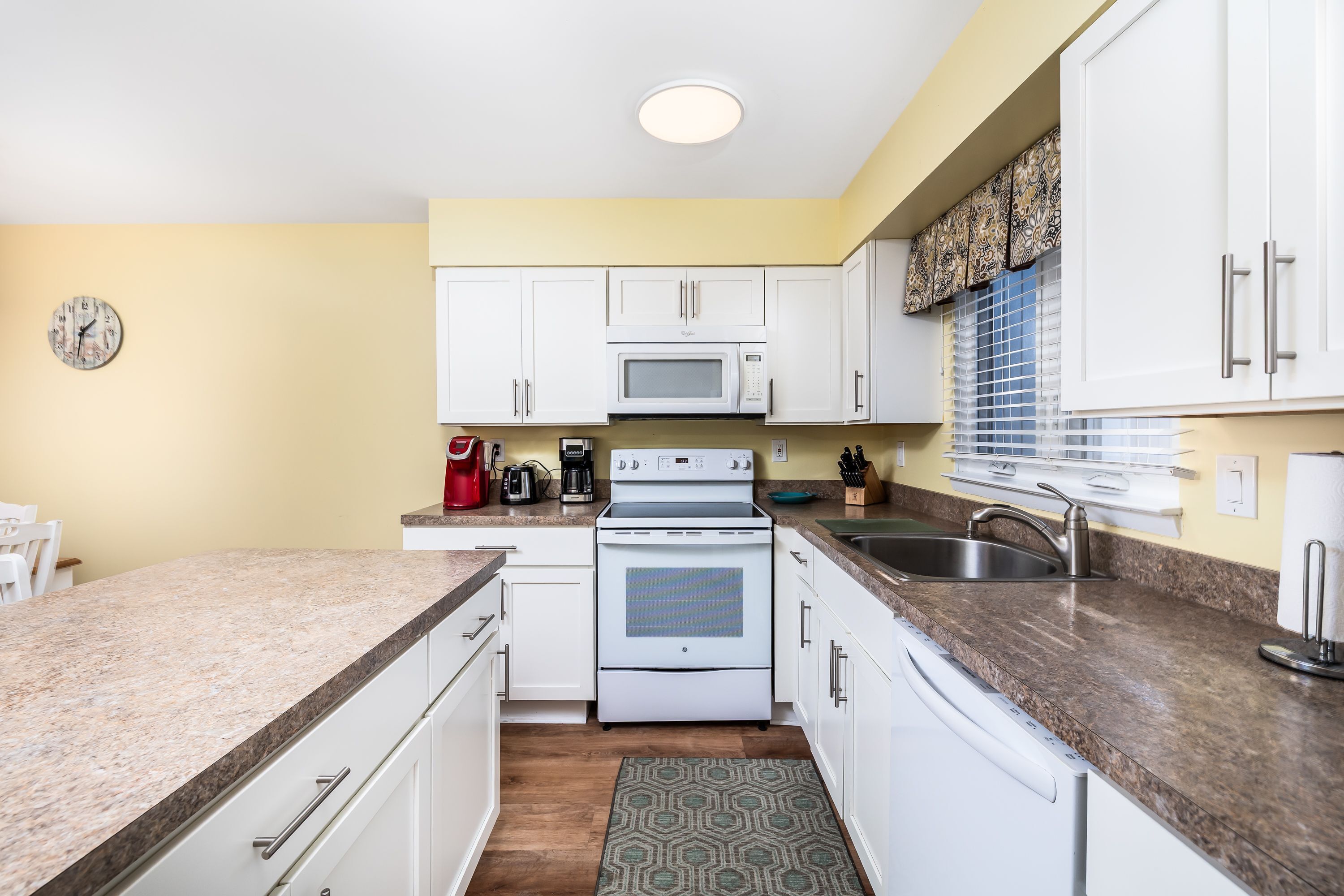 A kitchen with white cabinets, a microwave, stove, and a sink.