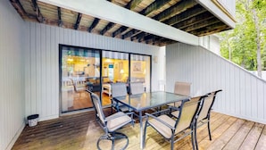 Un portico coperto con tavolo e sedie in vetro, pavimento in legno e vista sull'interno della casa.