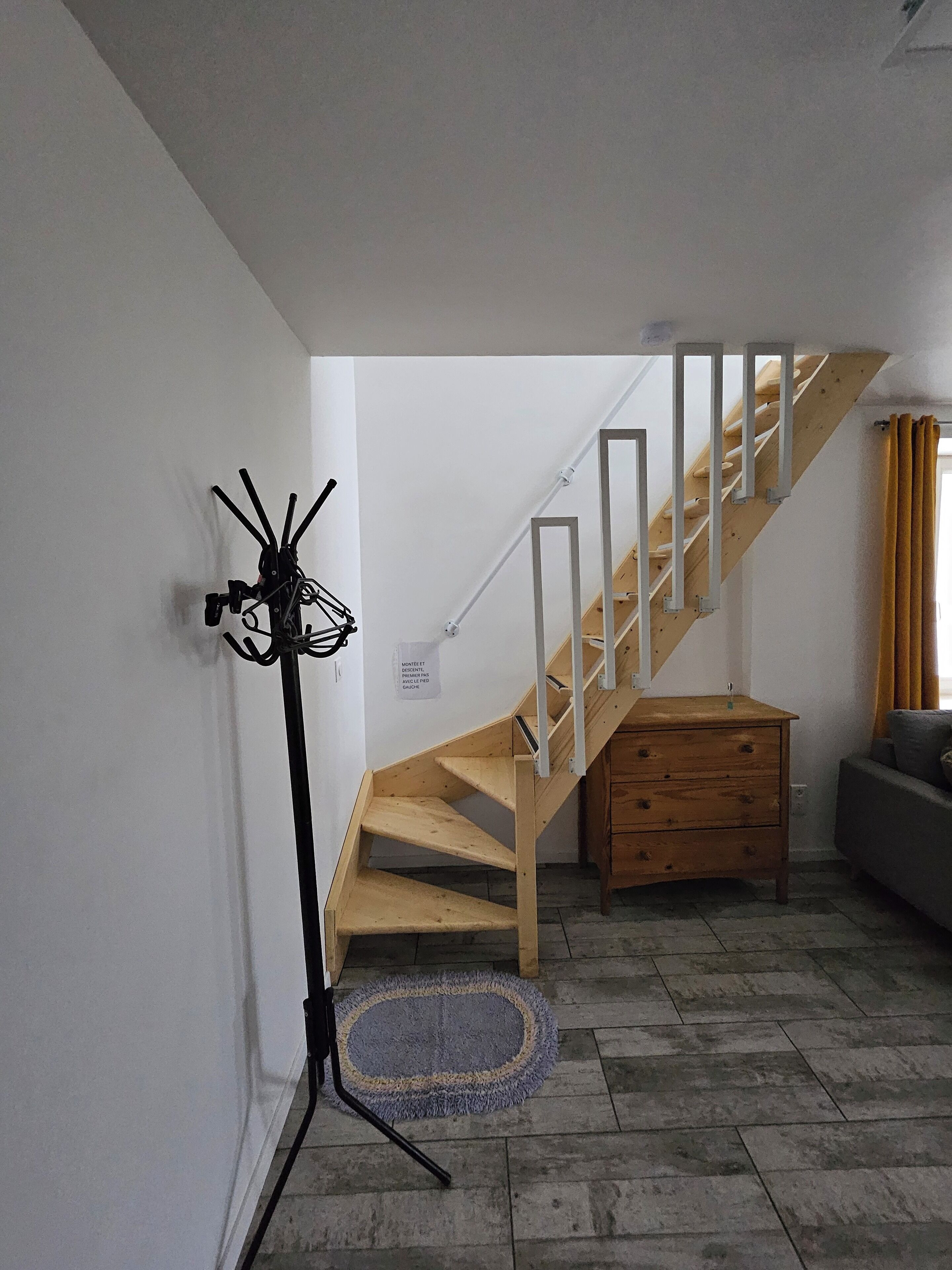 A staircase with wooden steps and white railings, a wooden dresser, and a floor lamp against a white wall.