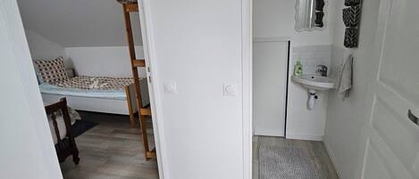 A compact room with a bunk bed, a small bathroom with a sink and mirror, and a wooden floor.
