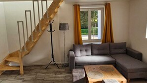 Un salon avec un escalier en bois, un canapé d’angle gris, une table basse et une lampe.
