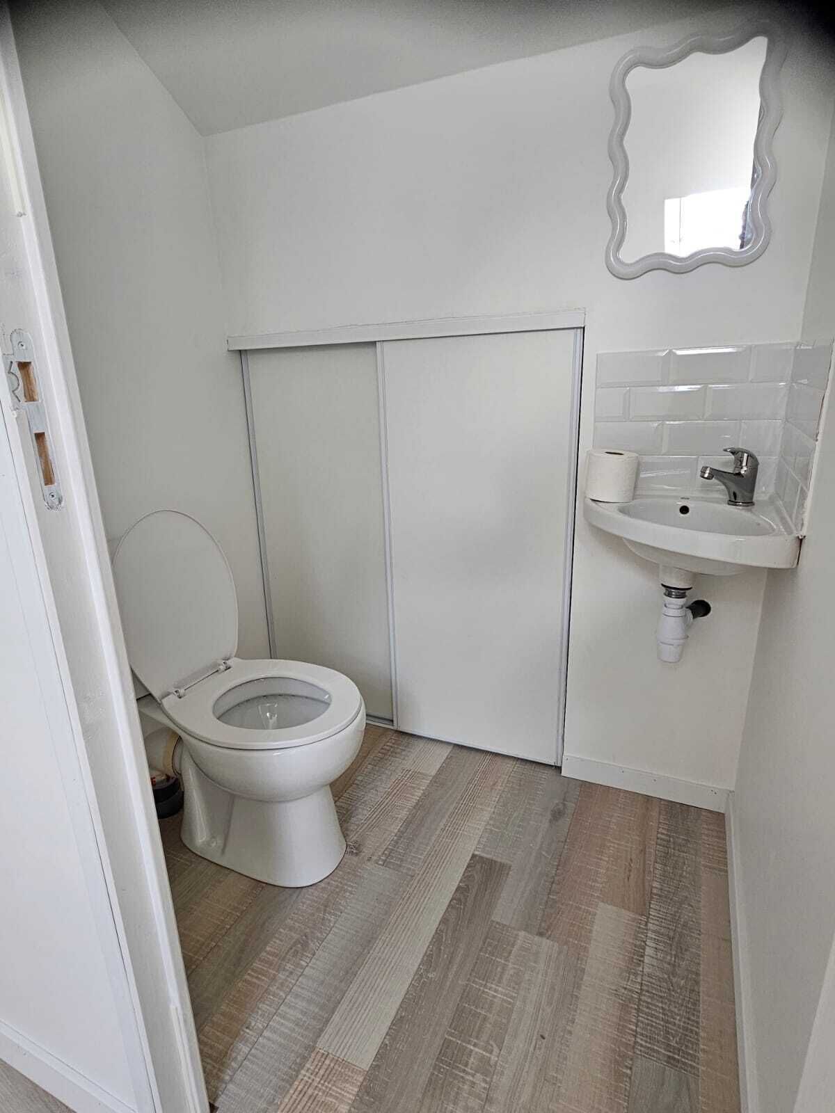 A small, compact bathroom with a toilet, sink, and mirror.