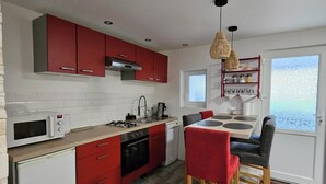 Une cuisine compacte avec des placards rouges, un four à micro-ondes, une cuisinière et un évier. On y trouve également un coin repas avec une table et des chaises.